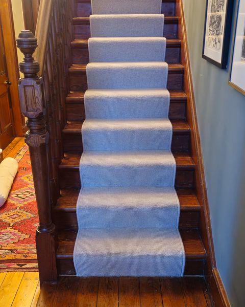 Grey stair runner on dark wood stairs with a carved newel post