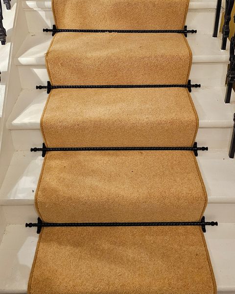 Gold stair runner held with black stair rods on white stairs