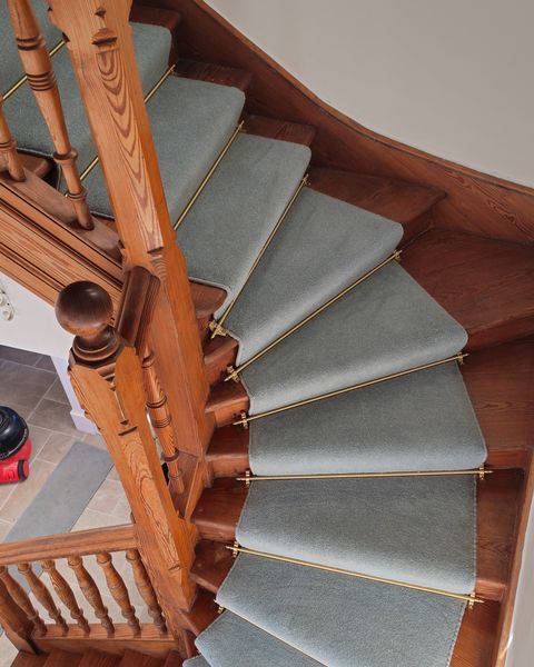 Grey runner on winding oak stairs with brass rods